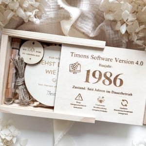 Könnte beinhalten: Eine Holzkiste mit Schiebedeckel, gefüllt mit kleinen Glasfläschchen, einer Holzscheibe und einer Holzplakette. Auf der Plakette steht "Timons Software Version 4.0, Baujahr: 1986." Zusätzlicher Text ist auf der Scheibe und in der Kiste sichtbar.