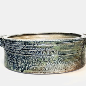 Puede incluir: Un plato de servir grande, redondo y de cerámica con dos asas. El plato está decorado con un esmalte azul y verde y tiene una superficie texturizada.