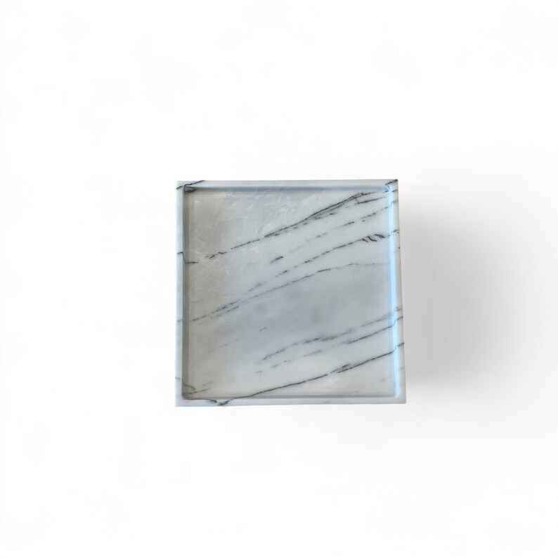 May include: Square marble tray with a white and gray veined pattern. The tray has a raised edge and is set against a white background. The marble has dark gray streaks.