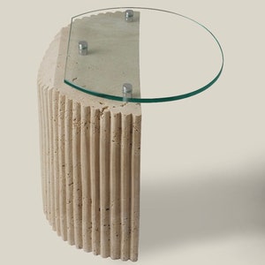 May include: A beige, fluted, half-round pedestal table with a clear glass top. The table has a modern design and is perfect for a living room or bedroom.