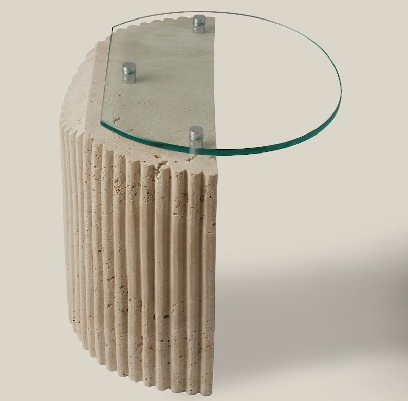 May include: A beige, fluted, half-round pedestal table with a clear glass top. The table has a modern design and is perfect for a living room or bedroom.