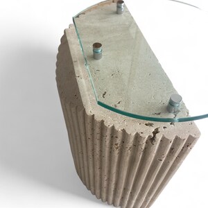 May include: A half-round side table with a fluted travertine base and a clear glass top. The table has three silver metal accents on the top.