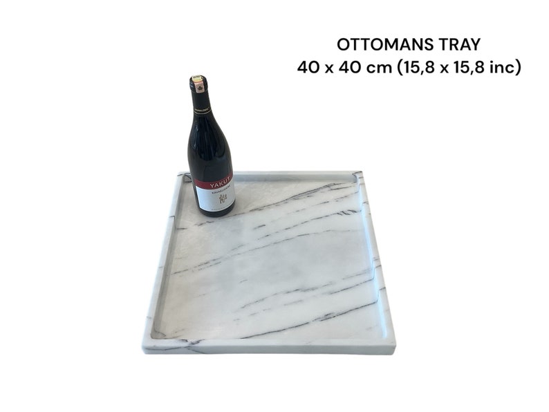 May include: A square marble-look ottoman tray, 15.8 x 15.8 inches, with a raised edge. A bottle of red wine rests on the tray. The tray has a white and gray veined pattern, and the text "OTTOMANS TRAY" is visible.