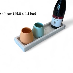 May include: A rectangular marble tray with a bottle of red wine and two ceramic cups. The tray measures 15.8 x 4.3 inches. One cup is peach-colored, and the other is light blue. The wine bottle has a white label with red text.