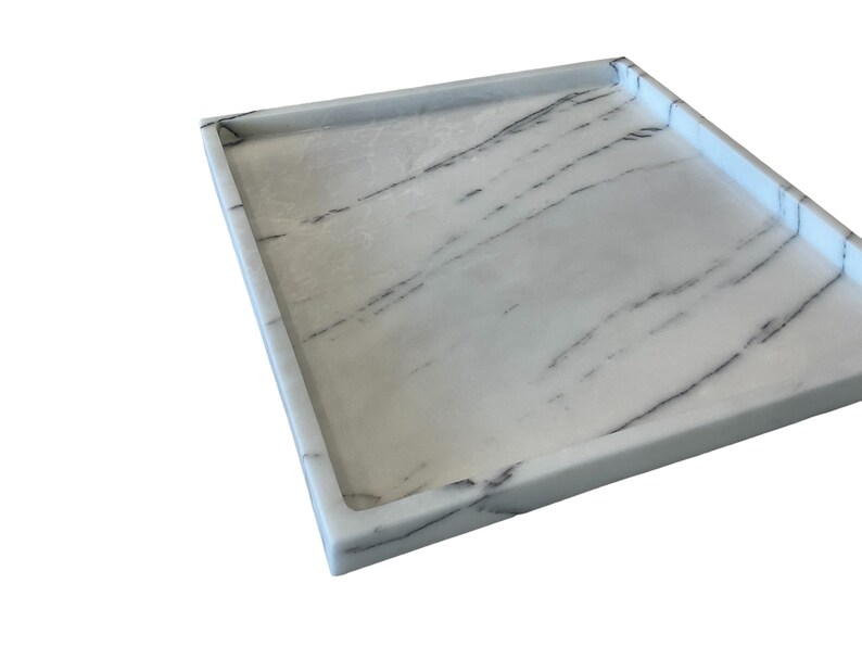 May include: A rectangular white marble tray with dark gray veining. The tray has a raised edge and a smooth surface. The marble pattern is consistent across the tray's surface, creating a cohesive design. The tray is suitable for serving or display.