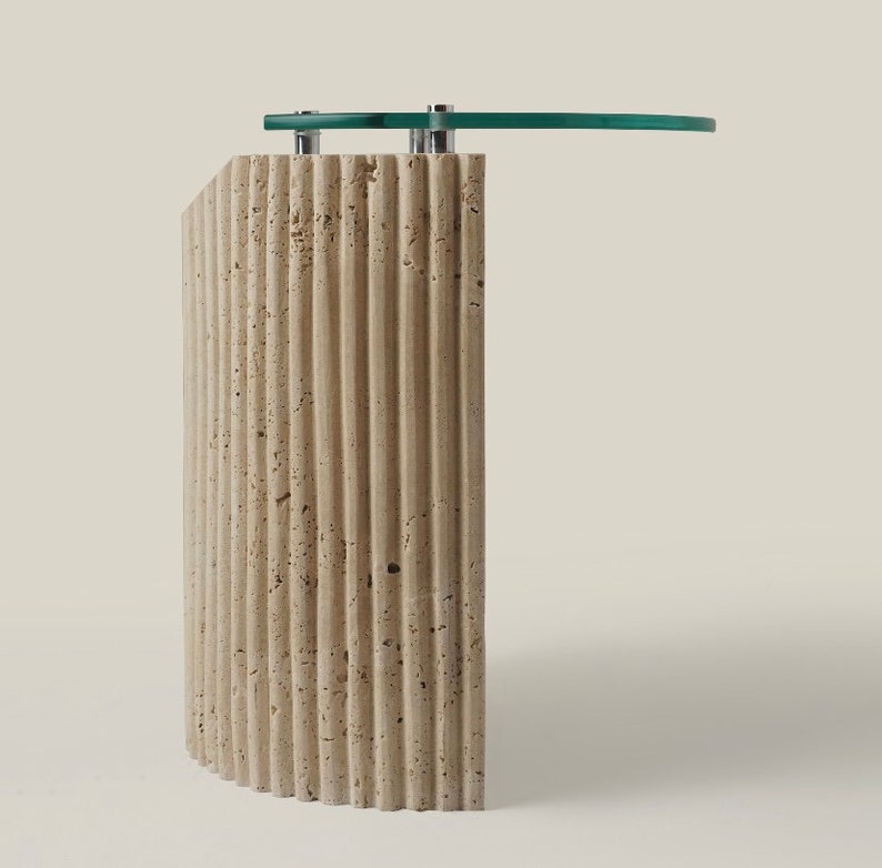 May include: A curved, beige travertine side table with a glass top. The table has a fluted design and a modern style.