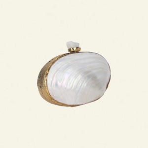 May include: A white, pearlescent clutch bag with a gold-coloured frame and clasp. The bag has a natural, shell-like appearance, with a textured gold border. A small, white stone adorns the top of the clasp. The design is elegant and sophisticated.