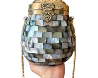 May include: A decorative, handcrafted purse with a mosaic pattern. The body of the purse is made of small, rectangular iridescent tiles in shades of gray, blue, and white. It has a gold-colored metal top and clasp, and a gold chain strap.