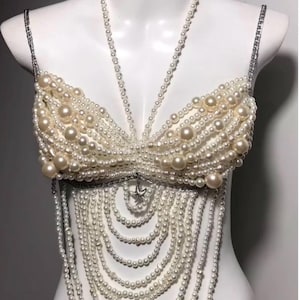 May include: A white pearl bra top with a long, layered pearl necklace. The bra top is made of many small pearls and has a delicate, feminine look.
