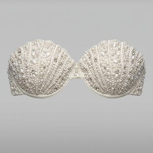 Può includere: Un reggiseno bianco senza spalline ricoperto di piccole perle rotonde e strass scintillanti. Il reggiseno ha un design a forma di conchiglia, con le perle disposte in file verticali. Un delicato ed elegante capo di lingerie.
