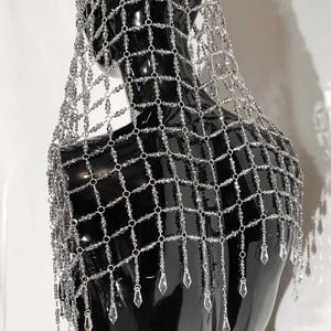 May include: A silver beaded headpiece with a net design and crystal-like accents. The headpiece has a fringe of dangling crystals.
