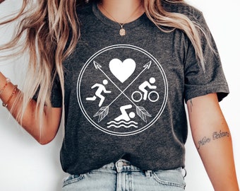 May include: Dark gray V-neck t-shirt featuring a white graphic of a heart, runner, cyclist, and swimmer within a circle. The design is crossed by arrows. The shirt is made of a soft material.