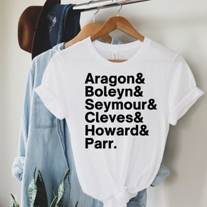 May include: White t-shirt with black text that reads "Aragon & Boleyn & Seymour & Cleves & Howard & Parr."
