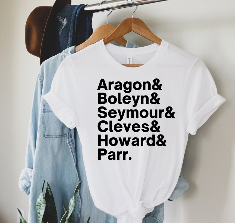 May include: White t-shirt with black text that reads "Aragon & Boleyn & Seymour & Cleves & Howard & Parr."