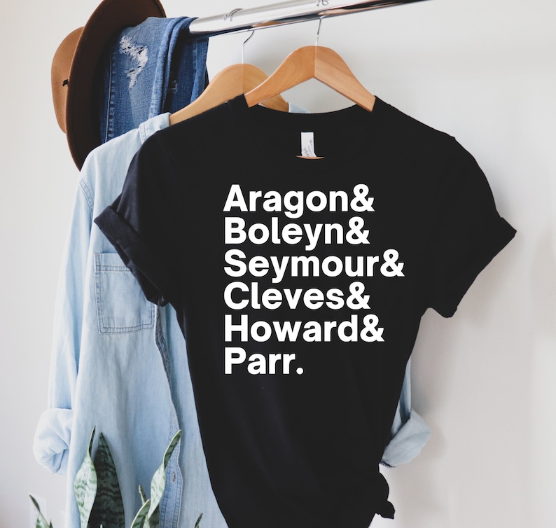 May include: Black t-shirt with white text that reads "Aragon & Boleyn & Seymour & Cleves & Howard & Parr."