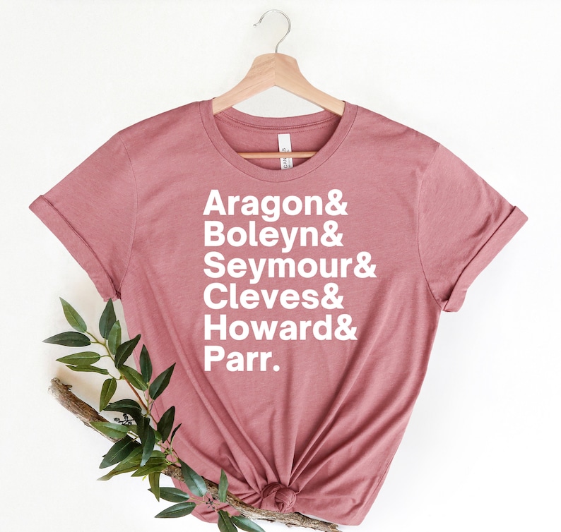 May include: A dusty rose t-shirt with white text that reads "Aragon & Boleyn & Seymour & Cleves & Howard & Parr."