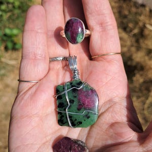 Pode incluir: Um anel de prata com uma pedra de rubi em zoisite, um pendente de rubi em zoisite envolto em fio metálico com uma argola e uma pequena peça de cristal de rubi vermelho escuro solta, apresentados juntos para mostrar as suas cores naturais.