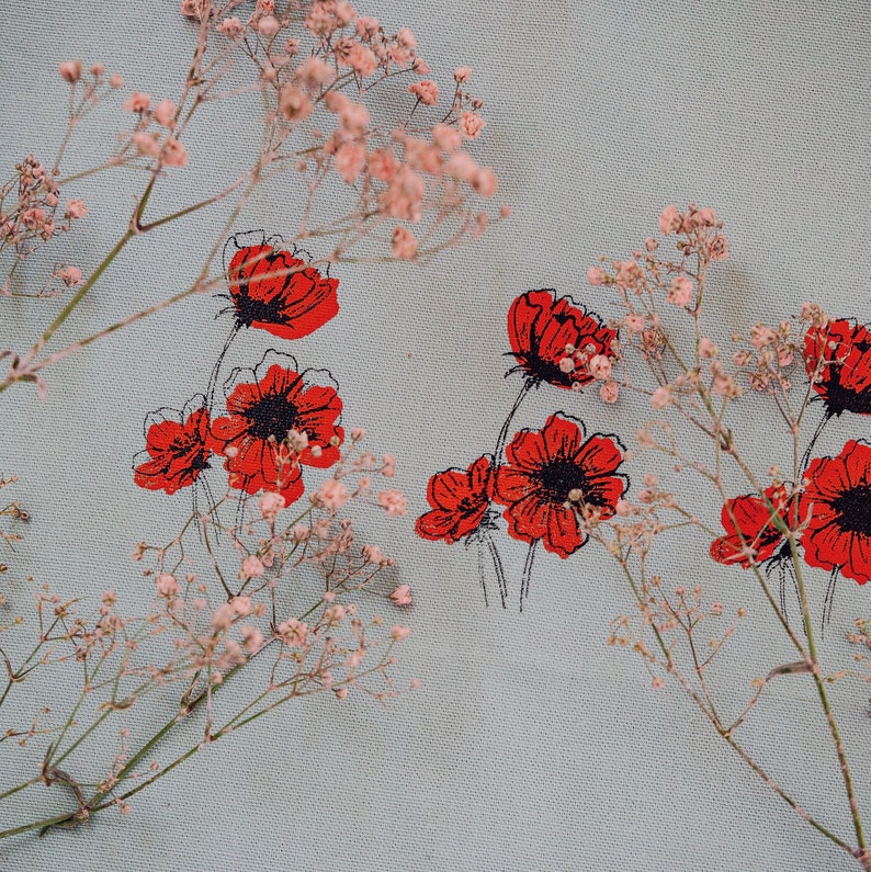 May include: A light blue fabric with a floral pattern featuring red poppy flowers and small pink flowers. The fabric has a subtle texture.