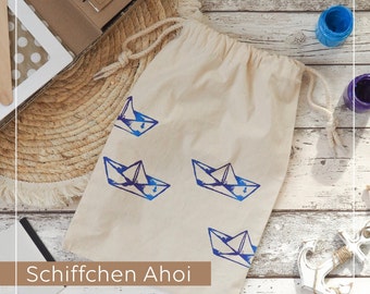 May include: A white canvas bag with blue paper boat designs and the text "Schiffchen Ahoi" printed on the front.
