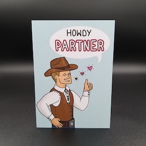 May include: A blue card featuring a cartoon cowboy wearing a brown hat and vest. The cowboy is giving a thumbs up and has a speech bubble above his head that says "Howdy Partner". There are small pink hearts floating around the speech bubble.