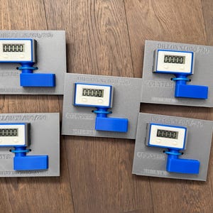 Pode incluir: Cinco contadores Dillon NL650/750 cinzentos e azuis com ecrãs digitais que mostram 00000. Cada contador está montado numa base cinzenta com o texto "DILLON NL650/750" e "COUNTER" impresso nele.