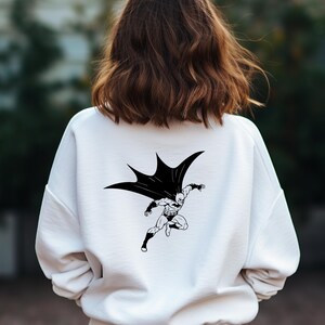 K&ouml;nnte beinhalten: Wei&szlig;er Pullover mit einem schwarz-wei&szlig;en Grafikdruck von Batman im Flug.