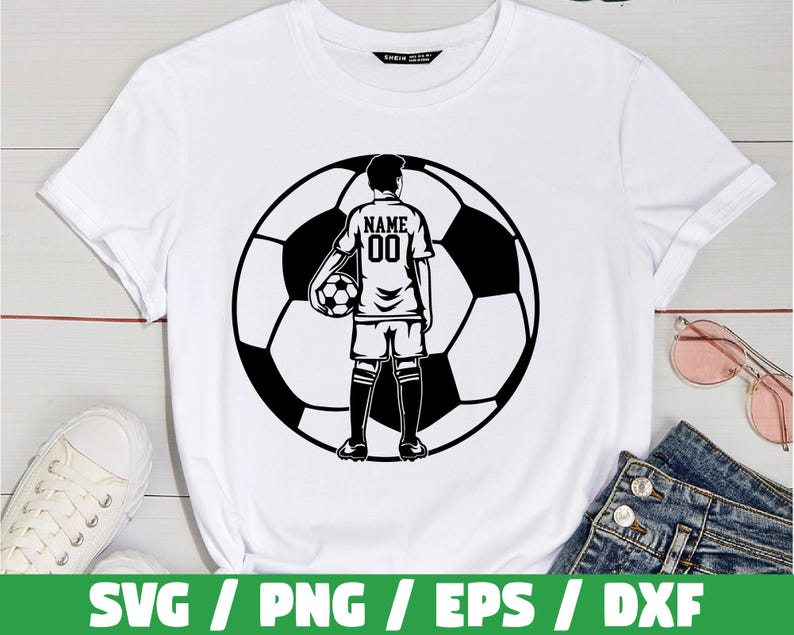Peut inclure: T-shirt blanc avec un graphisme noir et blanc d'un joueur de football tenant un ballon de football devant un ballon de football. Le maillot du joueur porte le mot "NAME" et le num&eacute;ro "00" au dos. Le t-shirt est pr&eacute;sent&eacute; sur une surface blanche.
