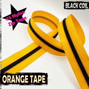 Puede incluir: Primer plano de una cinta de cremallera de nylon n.º 5 con una cinta naranja y una bobina negra. La cinta de cremallera está enrollada y doblada sobre un fondo blanco.  "BLACK COIL" y "ORANGE TAPE" están impresos en la imagen.