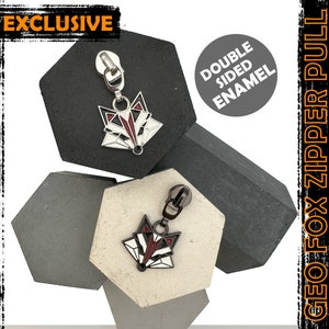 May include: Two silver zipper pulls featuring a geometric fox design. The fox is black, white and red. The zipper pulls are displayed on a grey and white background. The text "DOUBLE SIDED ENAMEL" and "GEO FOX ZIPPER PULL" are visible in the image.