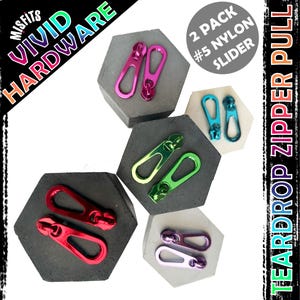 Puede incluir: Dos paquetes de deslizadores de cremallera de nylon n.º 5 en varios colores, incluidos rojo, verde, azul, morado y rosa. Los deslizadores tienen forma de lágrima y una lengüeta de arrastre. El embalaje dice "Misfits Vivid Hardware" y "2 Pack #5 Nylon Slider".
