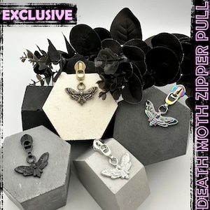 May include: Four different death moth zipper pulls, each with a different colour and design. The pulls are displayed on small hexagonal platforms. The text "EXCLUSIVE" is visible in the top left corner of the image.