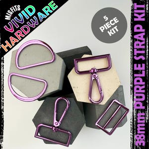 Puede incluir: Un kit de correas moradas de 5 piezas con anillas en D, un mosquetón giratorio, un deslizador rectangular y un anillo rectangular. El hardware se muestra sobre formas geométricas con el texto "Vivid Hardware" y "38mm Purple Strap Kit".