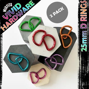May include: Two packs of 25mm D-rings in six different colours: green, red, blue, purple, orange, and pink. The D-rings are arranged on a grey background with the text "VIVID HARDWARE" and "2 PACK" visible.
