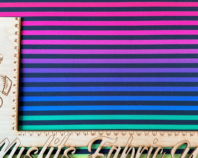 May include: A black and white striped fabric with horizontal stripes of pink, purple, blue, and green. The fabric is woven with a slight texture.