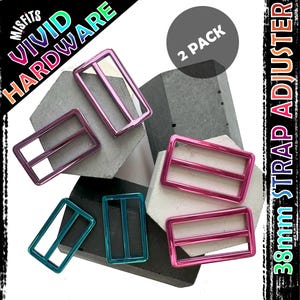 Puede incluir: Paquete de dos ajustadores de correa de 38 mm en rosa, turquesa y morado. Los ajustadores son de metal y tienen un acabado brillante. El producto está etiquetado como "VIVID HARDWARE" y "2 PACK".