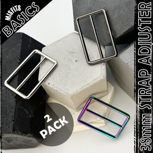 May include: Two 3/8 inch metal strap adjusters. One is silver and the other is iridescent. The adjusters are on a grey and black background. The text "MISFITS BASICS" and "3/8mm STRAP ADJUSTER" are visible in the image. The text "2 PACK" is also visible in the image.