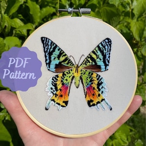 May include: Embroidered butterfly pattern in a wooden embroidery hoop. The butterfly is colorful with shades of blue, green, yellow, orange, red, and black.
