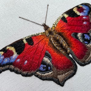 May include: A close-up of a red, black, and blue embroidered butterfly with detailed wings.