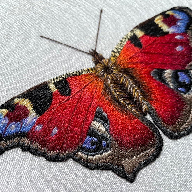 May include: A close-up of a red, black, and blue embroidered butterfly with detailed wings.