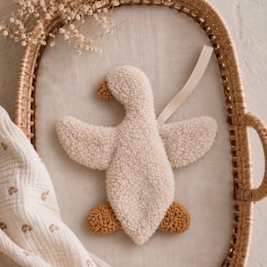 May include: A cream-coloured tufted goose-shaped wall hanging with a textured, looped pile surface. The goose features a brown beak and brown feet, with a light beige herringbone fabric loop attached to the back for hanging purposes.