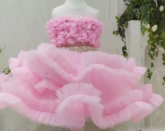May include: A pink tulle dress with a ruffled skirt and a flower-shaped bodice. The dress is on a white mannequin.