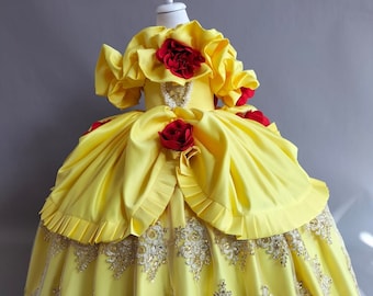 May include: A yellow satin ball gown with a lace overlay and red rose embellishments. The dress has a ruffled neckline and a full skirt.