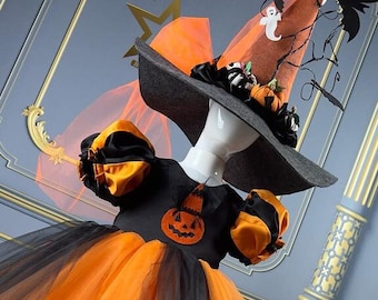May include: A black and orange tulle dress with a pumpkin applique and a black witch hat with orange and brown accents. The hat has a black spider web design and a small ghost figure.