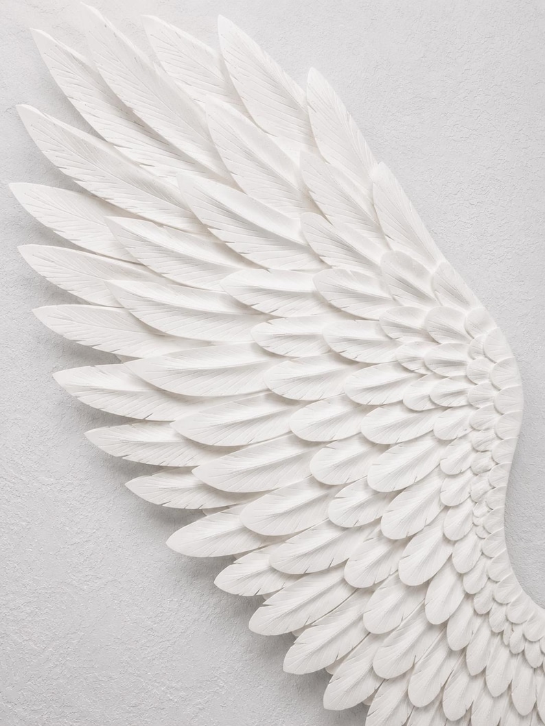 May include: A detailed, white, sculpted angel wing against a textured, light gray background. The wing is composed of layered, individual feathers, creating a sense of depth and texture. The feathers are intricately carved.