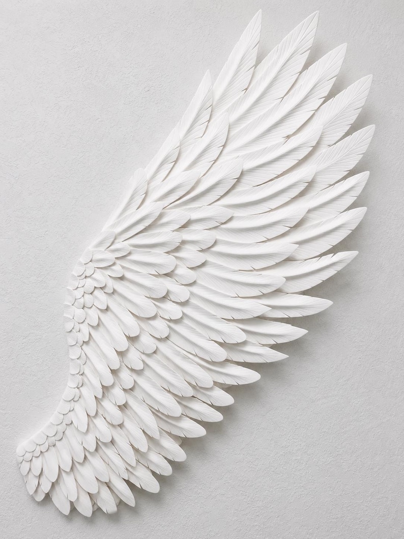 May include: A white, sculpted wing with detailed feather textures. The wing is a decorative piece, possibly for wall art or home decor. The feathers are layered, creating depth and a sense of movement. The overall design is clean and elegant.