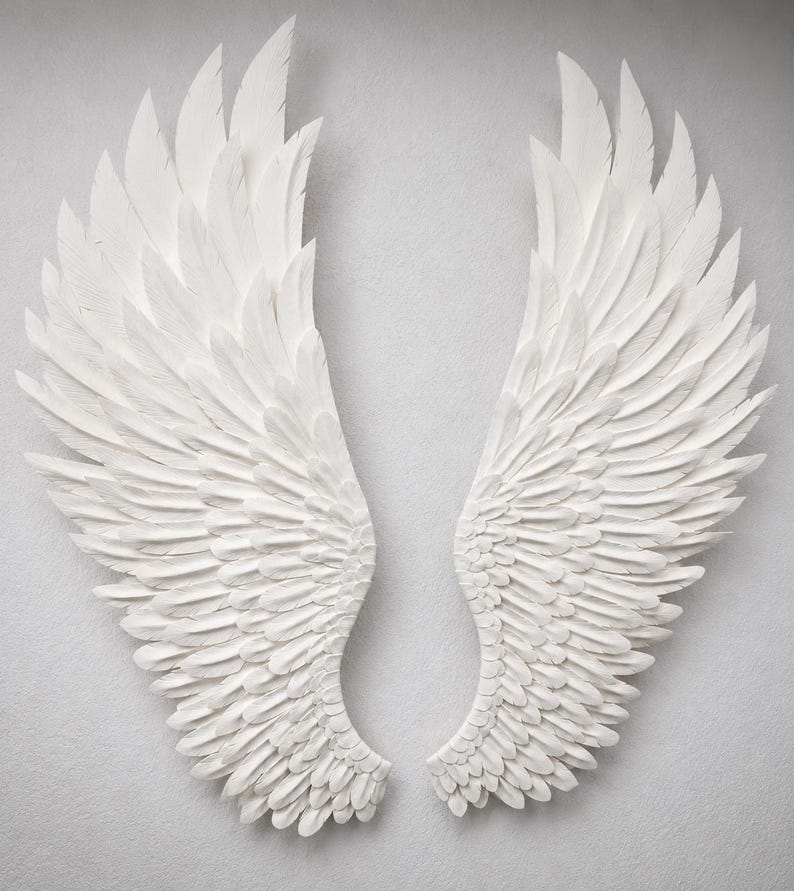 May include: Two large, white, sculpted angel wings. The wings are displayed side-by-side, with intricate feather detailing. The wings are a bright white color and appear to be made of a solid material.
