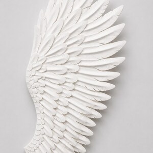 May include: A detailed, white, sculpted wing with layered feathers. The wing is a decorative piece, possibly for wall art or home decor. The feathers are intricately carved, creating a textured surface.