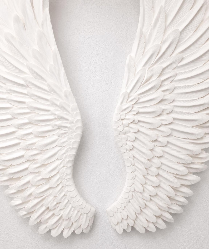 May include: A pair of white angel wings, each with detailed feather textures, are displayed against a plain white background. The wings are symmetrical, with a curved shape and a layered design, creating a sense of depth and dimension.