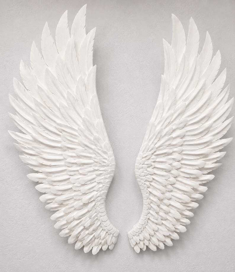 May include: A pair of white, sculpted angel wings, each with layered feather details. The wings are displayed against a neutral background, creating a striking contrast. The wings are a decorative item.