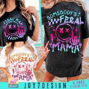 K&ouml;nnte beinhalten: Zwei schwarze T-Shirts mit einem grafischen Design eines Smiley-Gesichts mit gekreuzten Augen und dem Text "Somebody's Feral Mama" in Pink, Blau und Wei&szlig;.